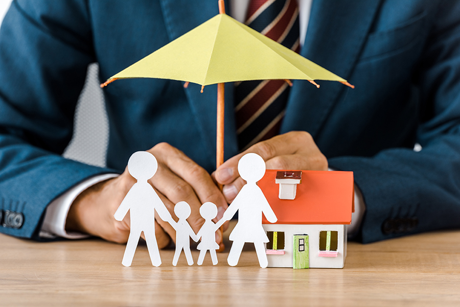 Male hands with paper cut family, house model and umbrella on wo