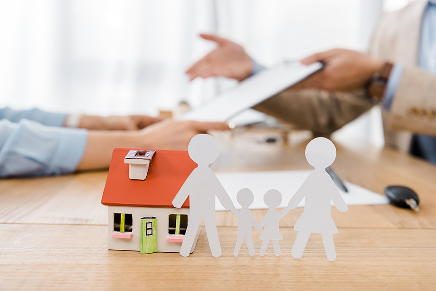 White paper cut family and house model on wooden table with blur